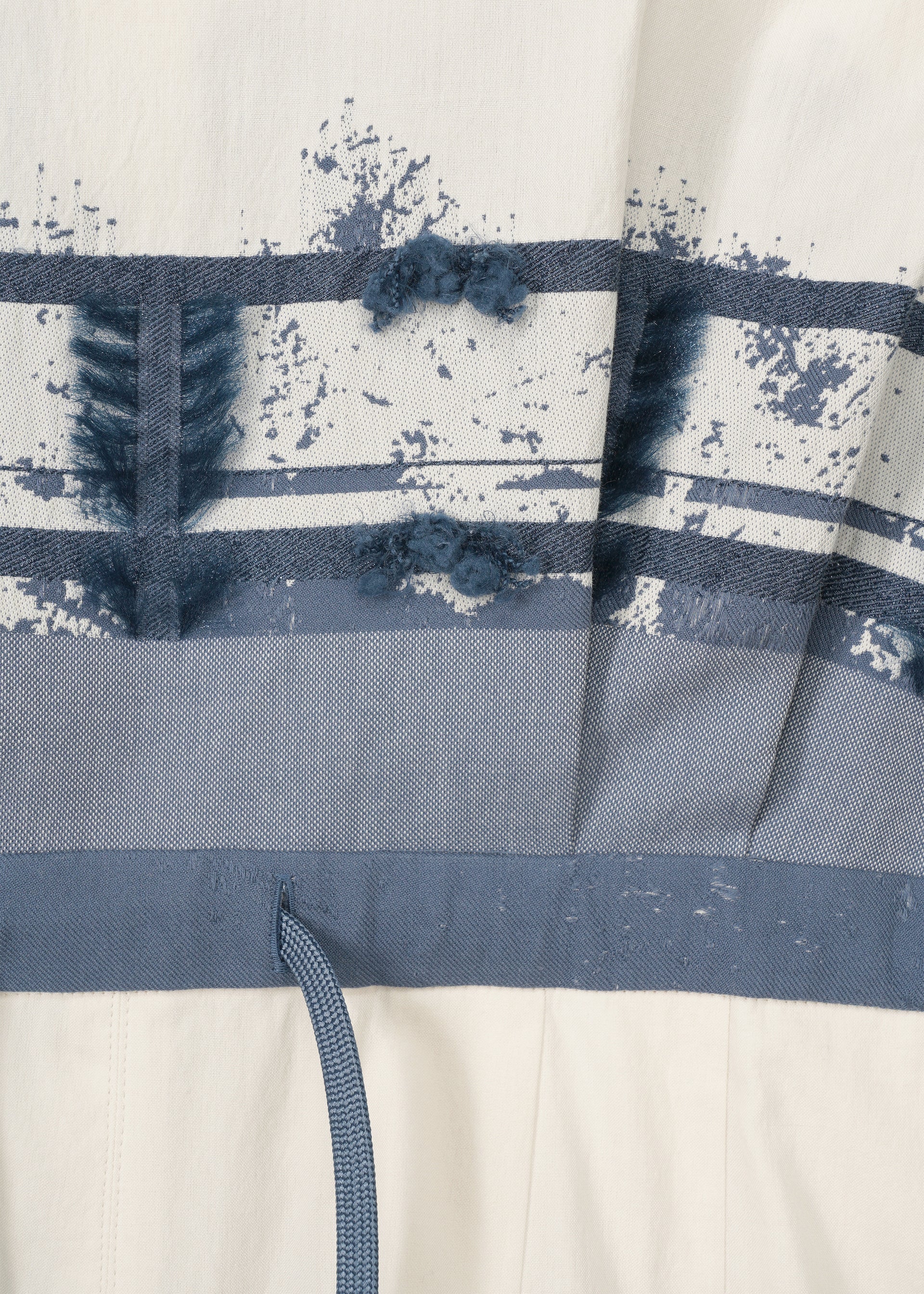 Zoomed view Close-up of the KASANEGAKE by HaaT: textured fabric with horizontal blue stripes and abstract blue patterns on white. Features a blue drawstring at the bottom, highlighting its layered design.