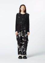 A person with long, wavy hair faces forward in the KOKUYU jumpsuit by HaaT, featuring expressive jacquard with white abstract paint splatters, loose-fitting pants, and black shoes against a plain white background.