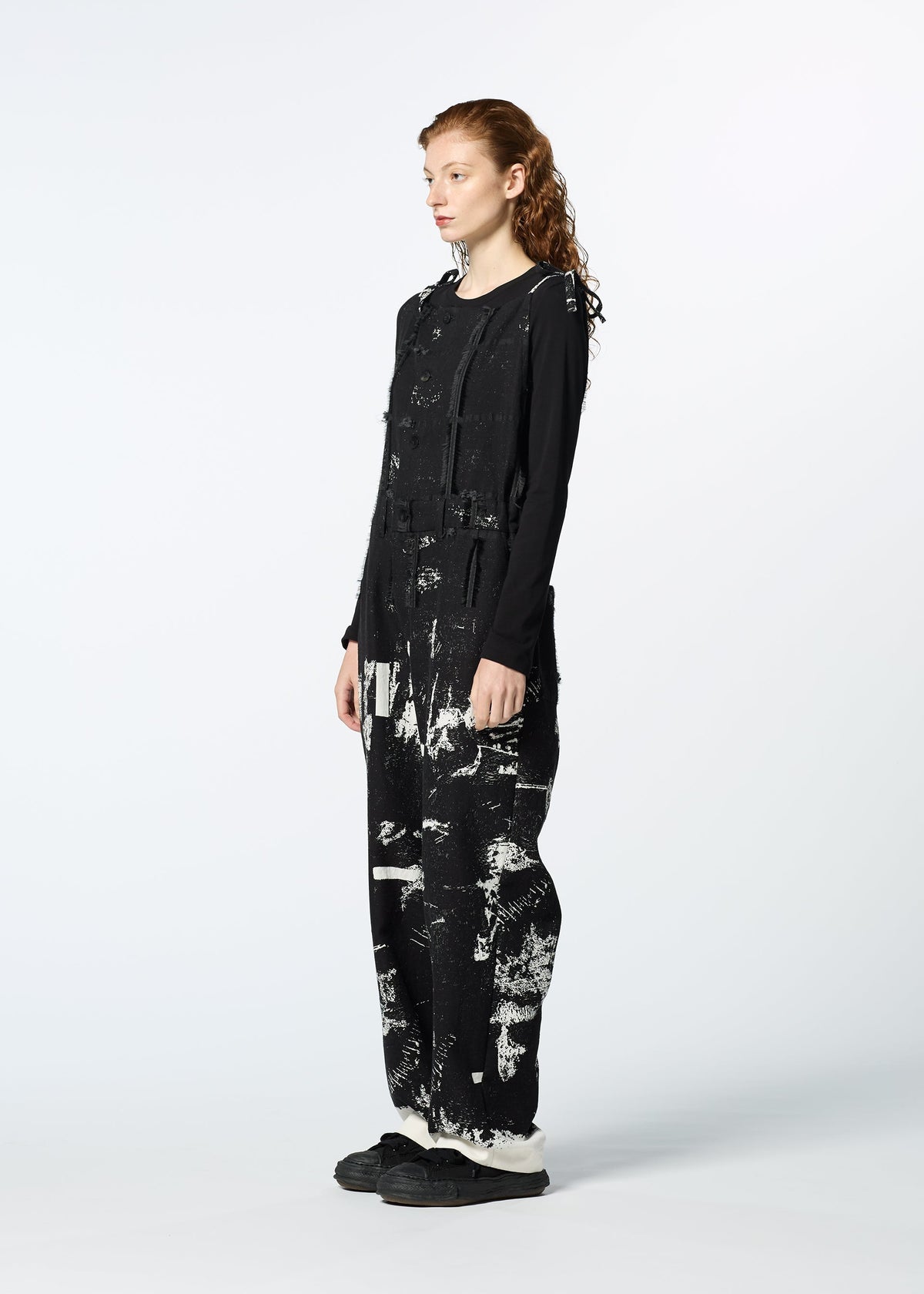 Wearing HaaT’s KOKUYU: a black long-sleeve top paired with an expressive jacquard jumpsuit featuring white abstract paint splatters, a person with long wavy red hair stands in profile against a plain light background. view 7 of 8