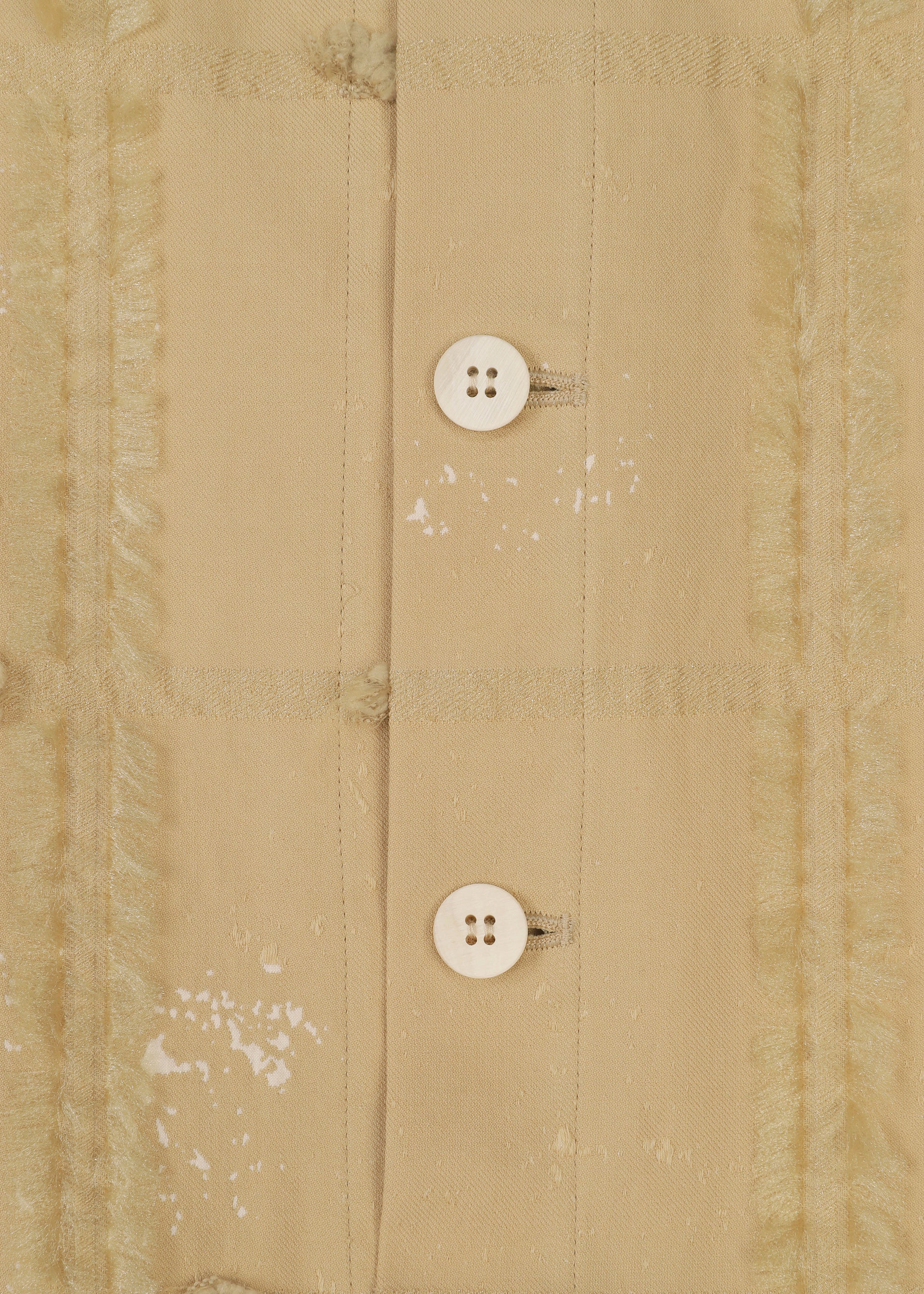Zoomed view Close-up of KOKUYU by HaaT shows beige fabric with two white four-hole buttons, frayed vertical seams, and faded textures, highlighting the expressive textile qualities typical of this jacquard jumpsuit.