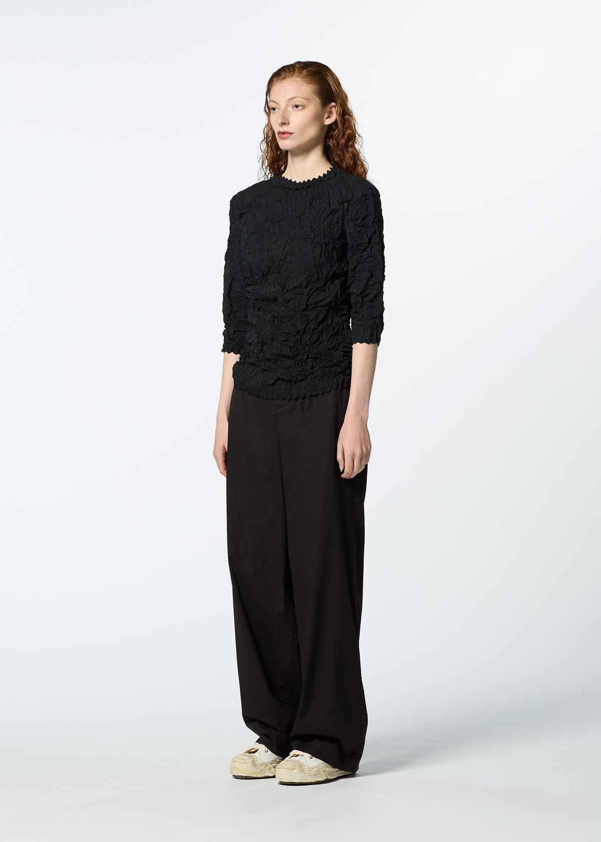 A person with long, wavy red hair stands in a studio wearing the KUMO SHIBORI SHIRT by HaaT, styled with loose black pants and white sneakers, facing slightly to the side against a plain white background. view 8 of 9