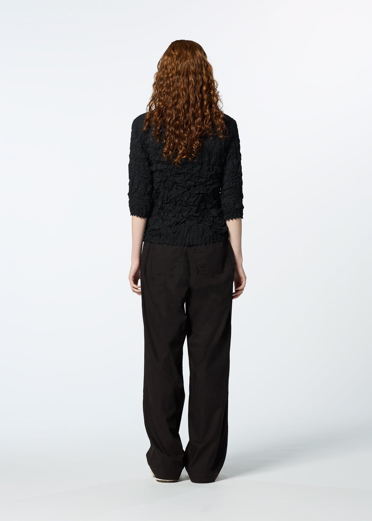 A person with long, curly auburn hair faces away, wearing the HaaT KUMO SHIBORI SHIRT with three-quarter sleeves and loose black pants against a plain white background. view 9 of 9