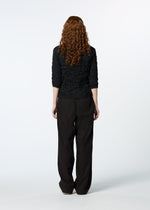 A person with long, curly auburn hair faces away, wearing the HaaT KUMO SHIBORI SHIRT with three-quarter sleeves and loose black pants against a plain white background.