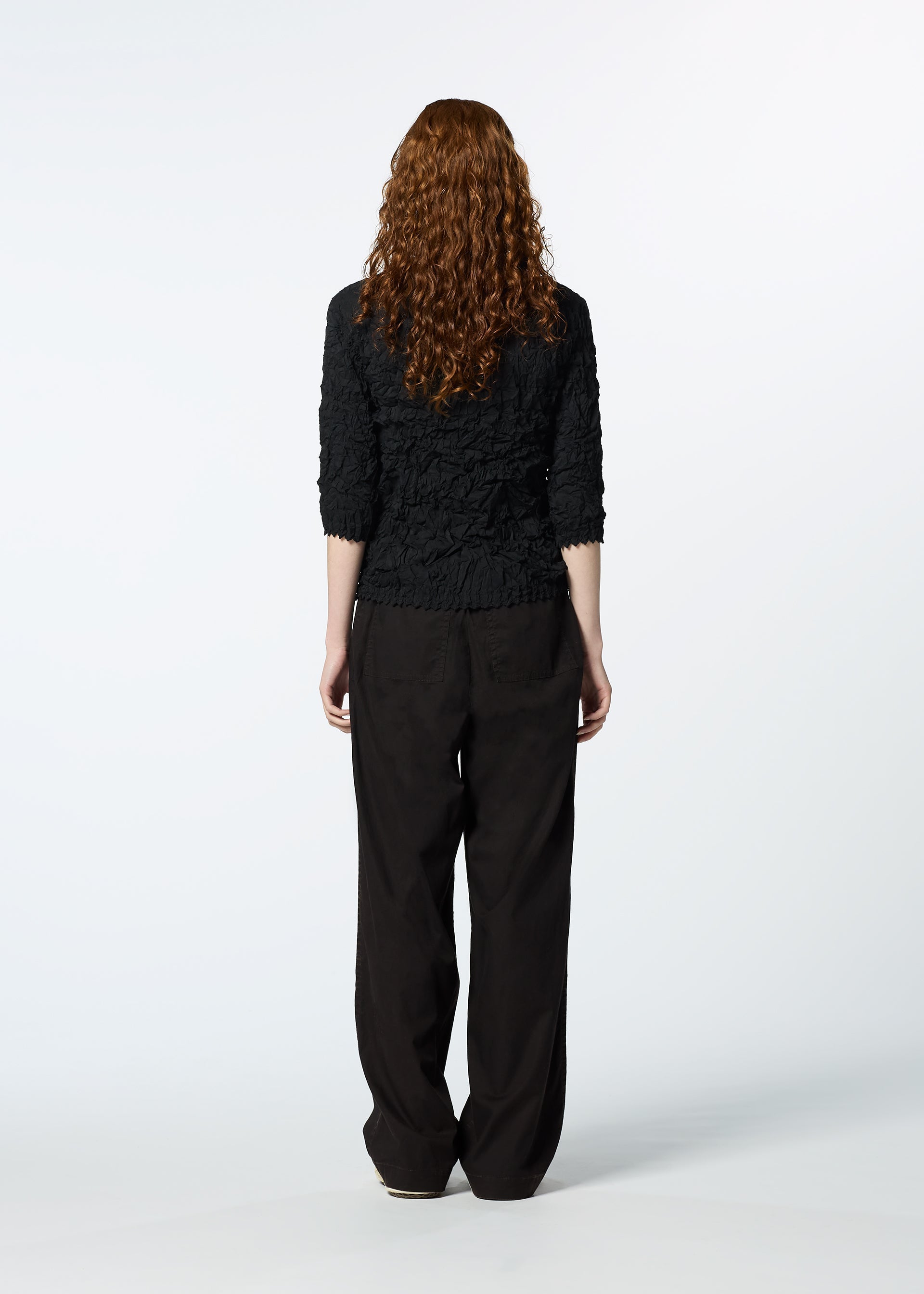 Zoomed view A person with long, curly auburn hair faces away, wearing the HaaT KUMO SHIBORI SHIRT with three-quarter sleeves and loose black pants against a plain white background.
