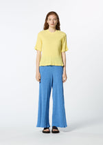 A person stands against a plain white background wearing a textured yellow KYO CHIJIMI MAY round-neck top from HaaT, loose blue wide-leg pants, and black sandals.