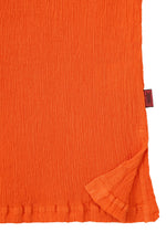 A close-up of the textured orange fabric from the HaaT KYO CHIJIMI MAY top, highlighting its ultra-fine cotton weave, slightly crinkled surface, a folded corner, and a small red tag on the edge.