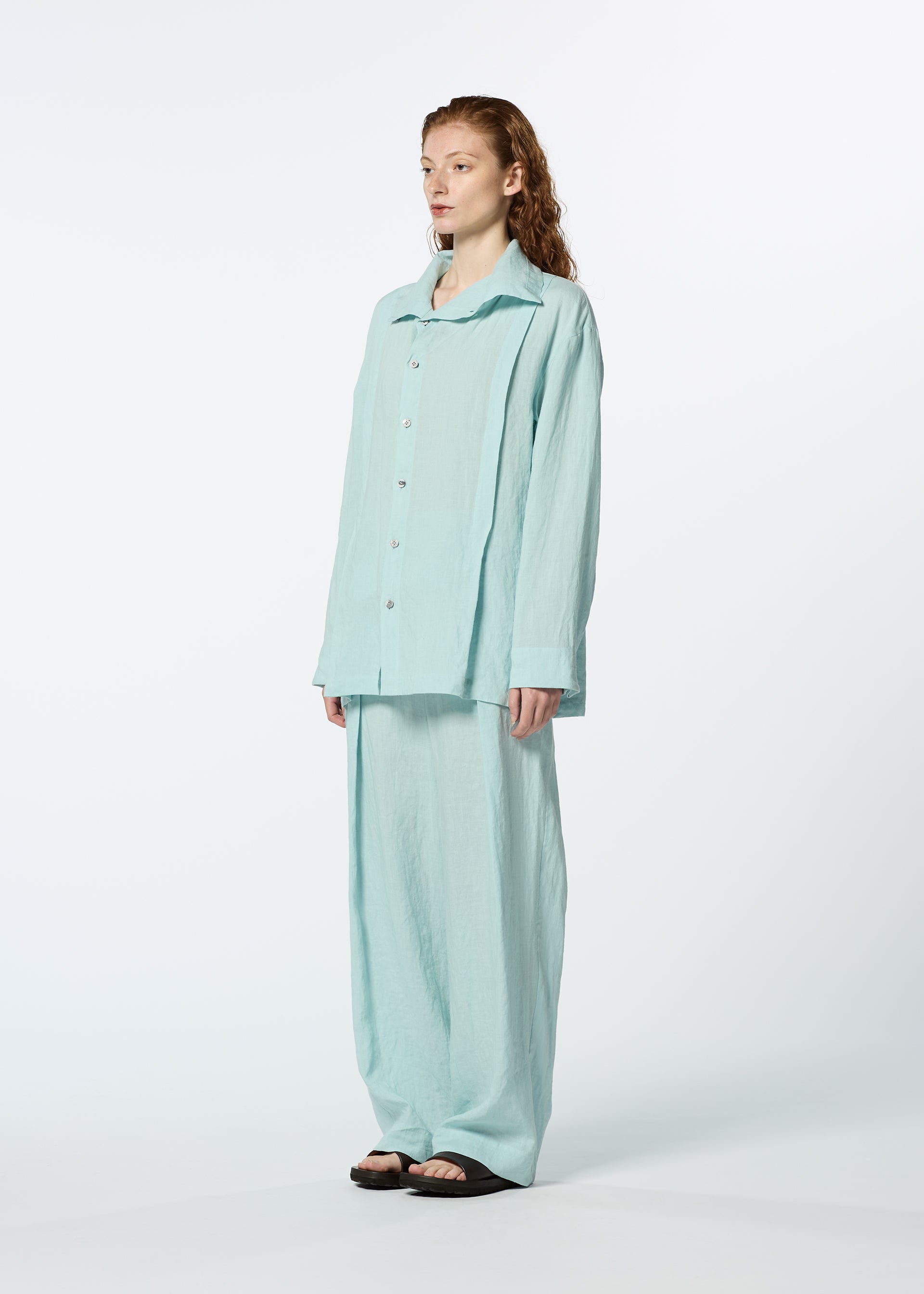 Zoomed view A red-haired model stands in a studio wearing HaaT's JIKI women's blouse and matching wide-leg pants with black sandals. The light blue outfit pops beautifully against the plain white background.