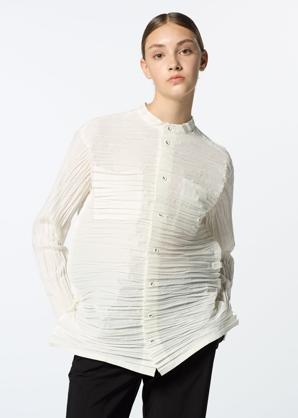 A young woman with brown hair slicked back wears the HaaT SHIBARI SHIRT, a white, long-sleeved top made from recycled polyester, paired with black pants. She stands against a plain white background with a neutral expression. view 10 of 10