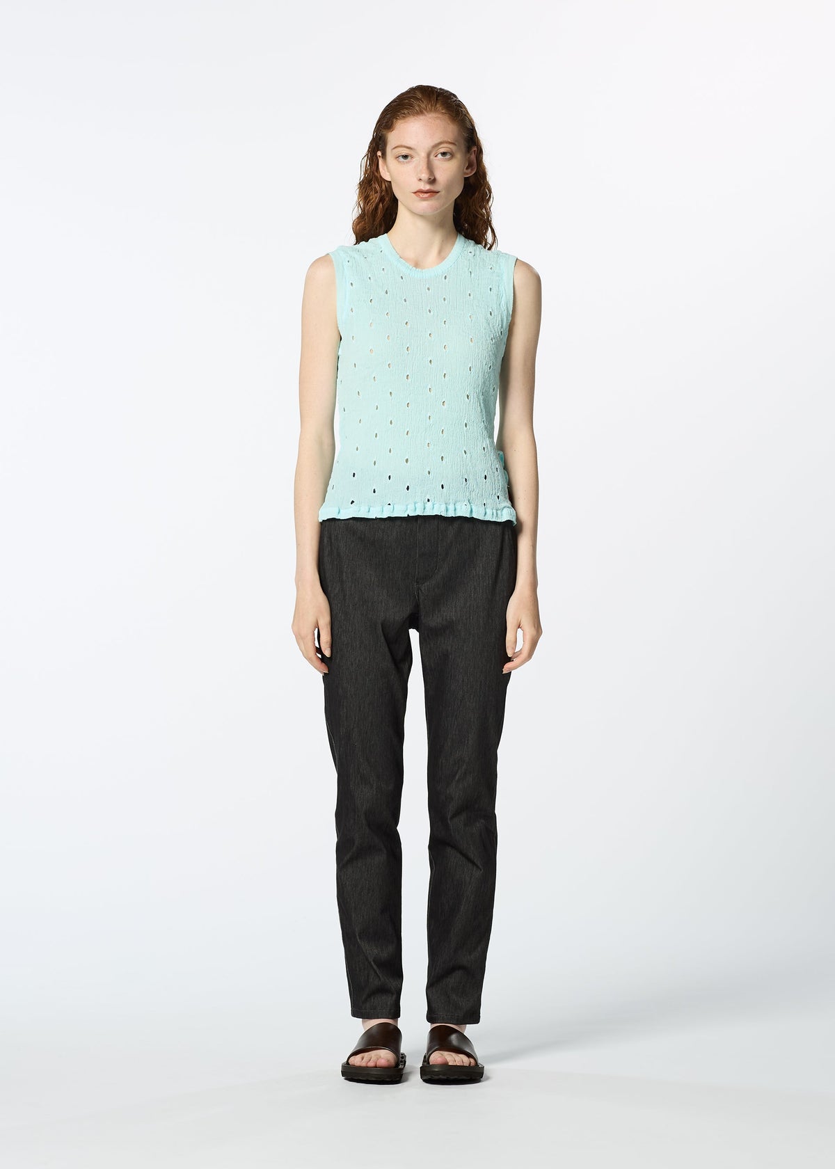 A woman with long, wavy hair wears the HaaT KYO CHIJIMI TOBIKANNA CADEAU sleeveless light blue top, dark pants, and black sandals, standing against a plain white background. view 8 of 10