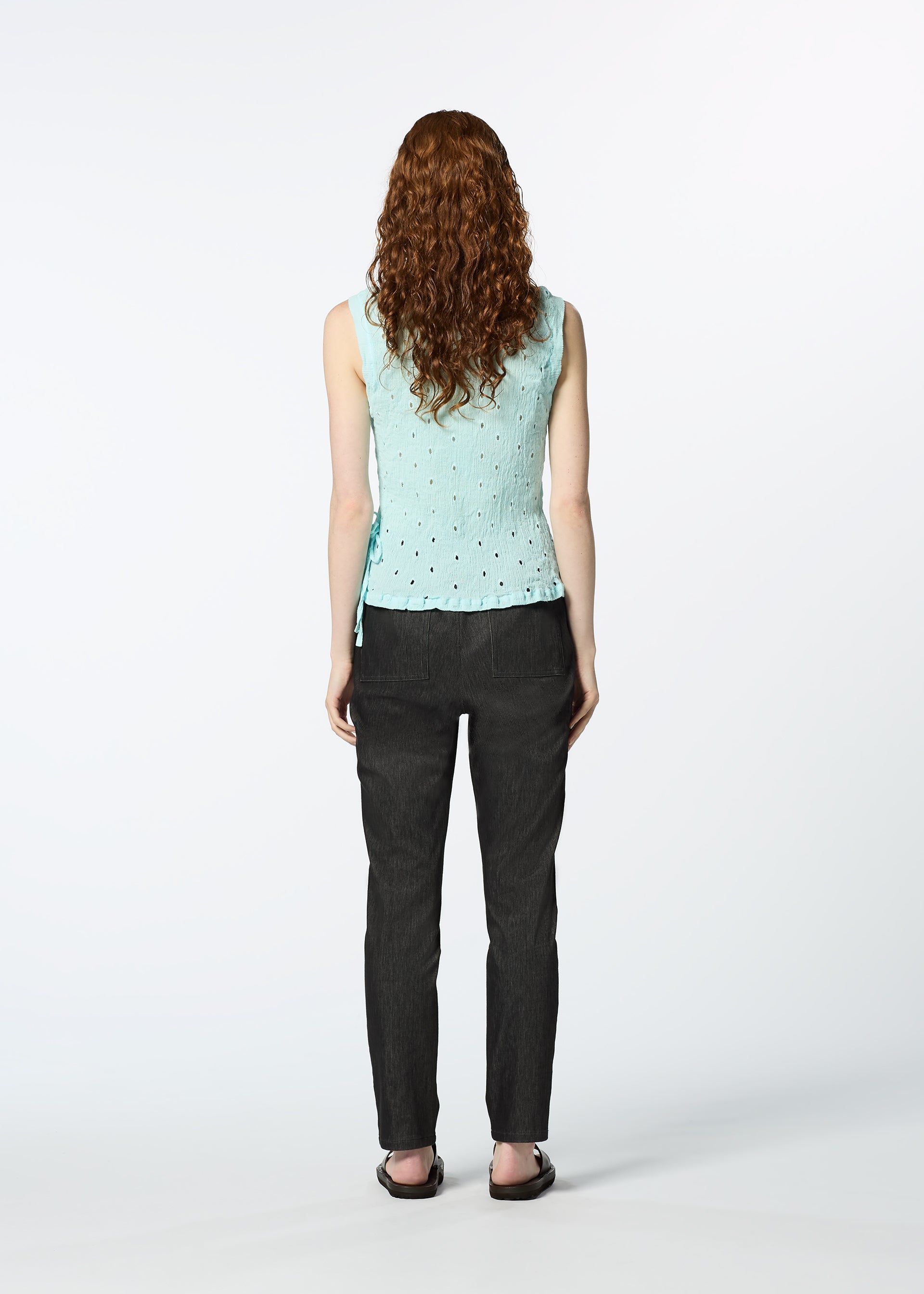 Zoomed view A person with long curly hair, dressed in a light blue HaaT KYO CHIJIMI TOBIKANNA CADEAU sleeveless top, dark pants, and black sandals, stands facing away against a plain white background.