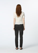 A person with long, curly hair stands facing away, wearing the HaaT KYO CHIJIMI TOBIKANNA CADEAU short-sleeve top, dark pants, and flat shoes against a plain white background.