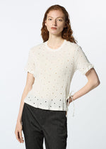 A person with long red hair wears the KYO CHIJIMI TOBIKANNA CADEAU white short-sleeve top by HaaT, featuring Tobikanna embroidery and ruffled edges, paired with dark pants against a plain light background.