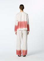 A person faces away, wearing the HaaT SAZANAMI top—an organic cotton piece hand-painted with vibrant pink and orange horizontal brushstrokes on the back and cuffs. The background is plain white.
