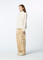 A person with long, wavy hair stands sideways against a plain light background, wearing HaaT's KYO CHIJIMI 2WAY JANUARY 1 high-neck sweater and wide beige patterned pants, paired with cream sneakers.