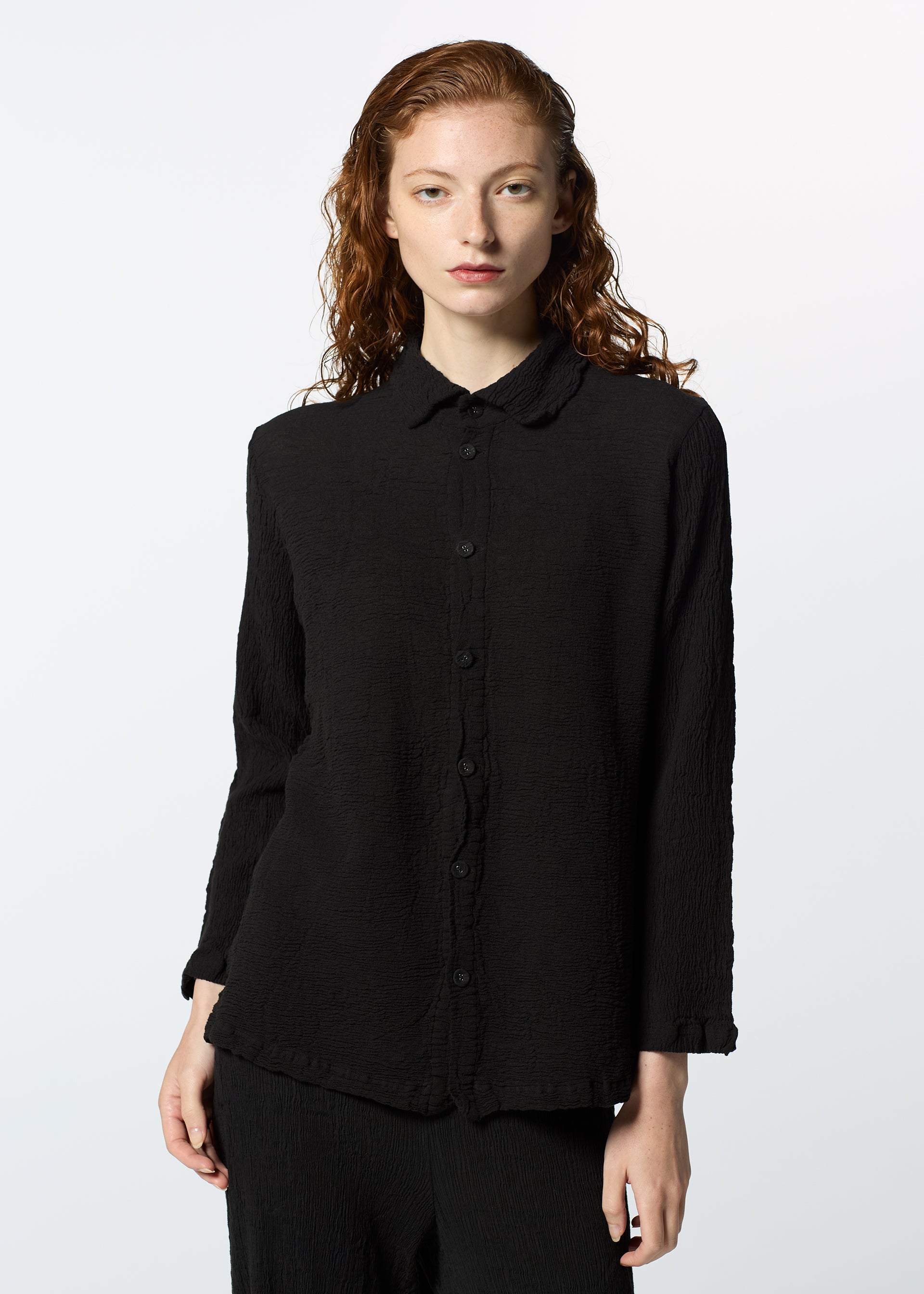 Zoomed view A person with long, wavy red hair wears the HaaT KYO CHIJIMI 2WAY JANUARY 1 shirt in black and black pants, standing against a plain light background and gazing directly at the camera with a neutral expression.