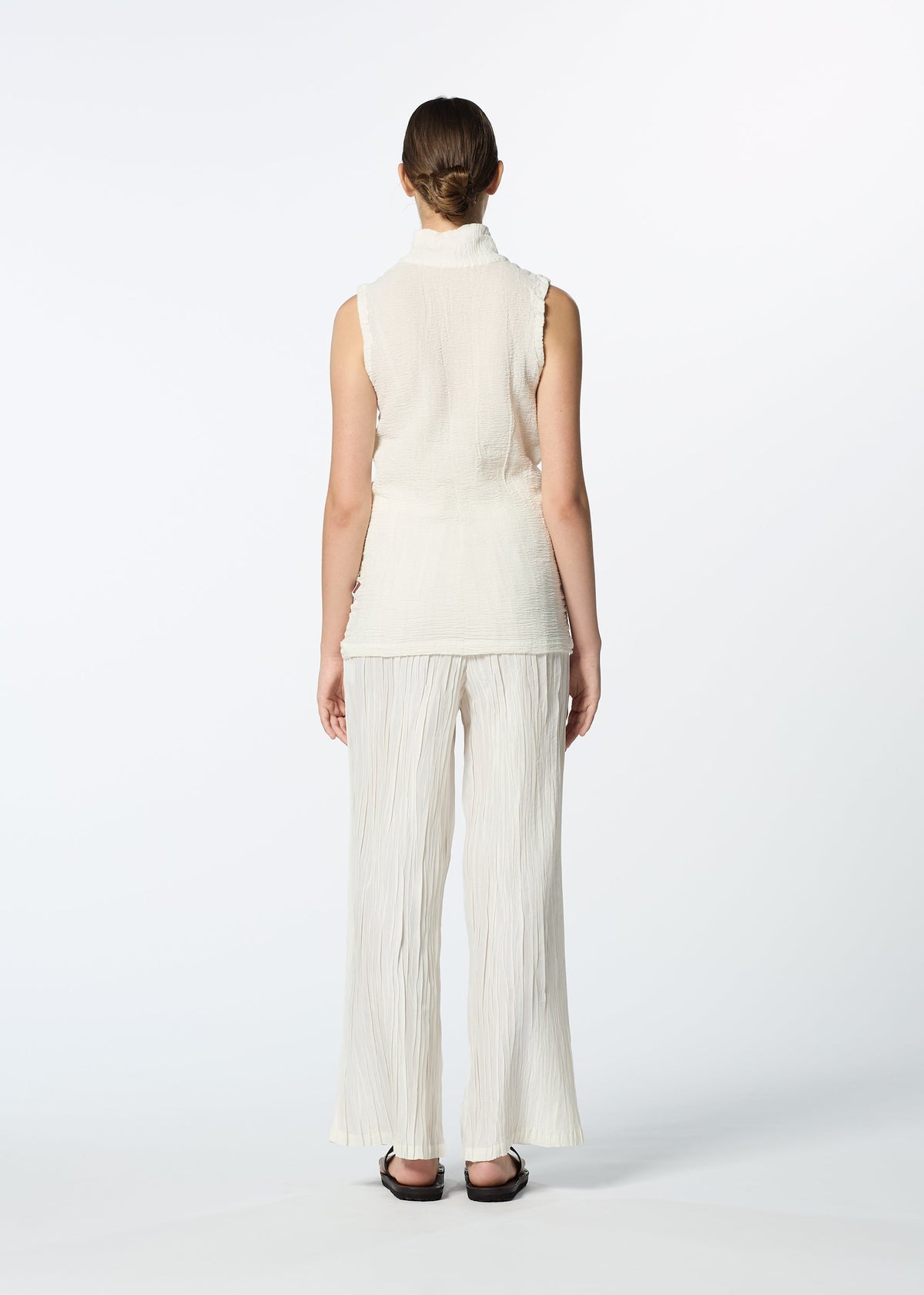 A person with brown hair in a low bun stands with their back to the camera, wearing the HaaT KYO CHIJIMI 2WAY JUNE 1 set—high-neck sleeveless top and matching wide-leg pants—with black sandals, against a white background. view 7 of 7
