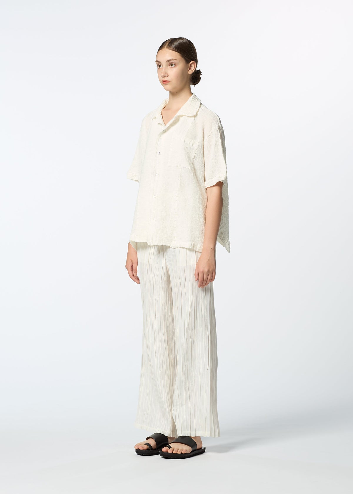 A young woman poses in HaaT's KYO CHIJIMI 2WAY JUNE 1, featuring a loose open-collar shirt, wide-leg pleated cream pants, and black sandals against a plain white background. view 6 of 7