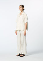 A young woman poses in HaaT's KYO CHIJIMI 2WAY JUNE 1, featuring a loose open-collar shirt, wide-leg pleated cream pants, and black sandals against a plain white background.