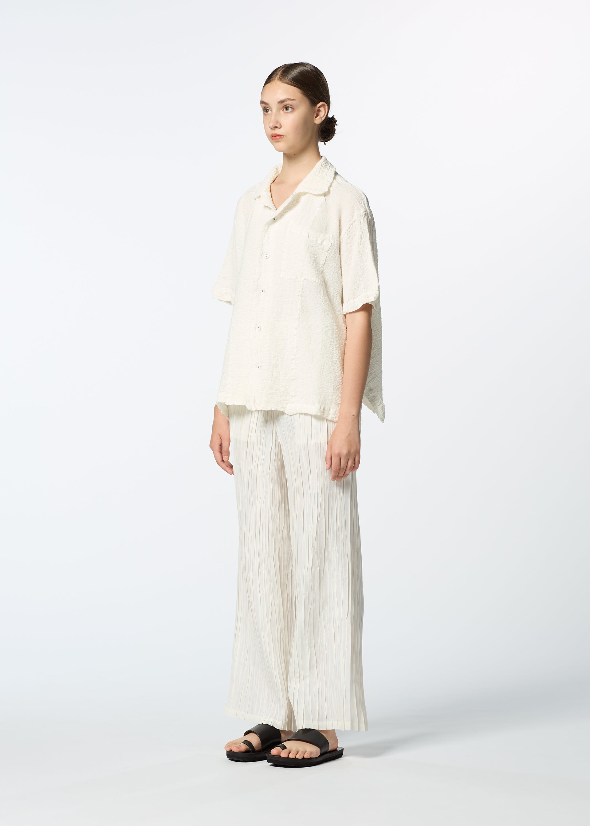 Zoomed view A young woman poses in HaaT's KYO CHIJIMI 2WAY JUNE 1, featuring a loose open-collar shirt, wide-leg pleated cream pants, and black sandals against a plain white background.