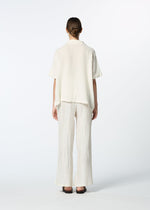 A person faces away, dressed in the HaaT KYO CHIJIMI 2WAY JUNE 1 short-sleeved shirt and wide, pleated, off-white pants with black sandals against a plain white background.