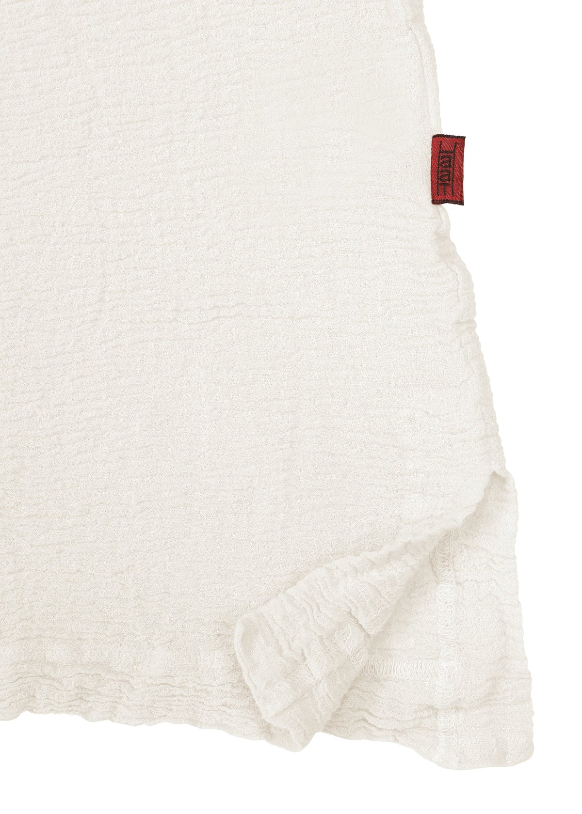 A close-up of the white textured fabric from the HaaT KYO CHIJIMI 2WAY JUNE 1 shirt highlights a slightly ruffled edge and a small red tag on the upper right seam, showcasing details created by product dyeing. view 4 of 7