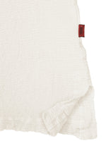 A close-up of the white textured fabric from the HaaT KYO CHIJIMI 2WAY JUNE 1 shirt highlights a slightly ruffled edge and a small red tag on the upper right seam, showcasing details created by product dyeing.
