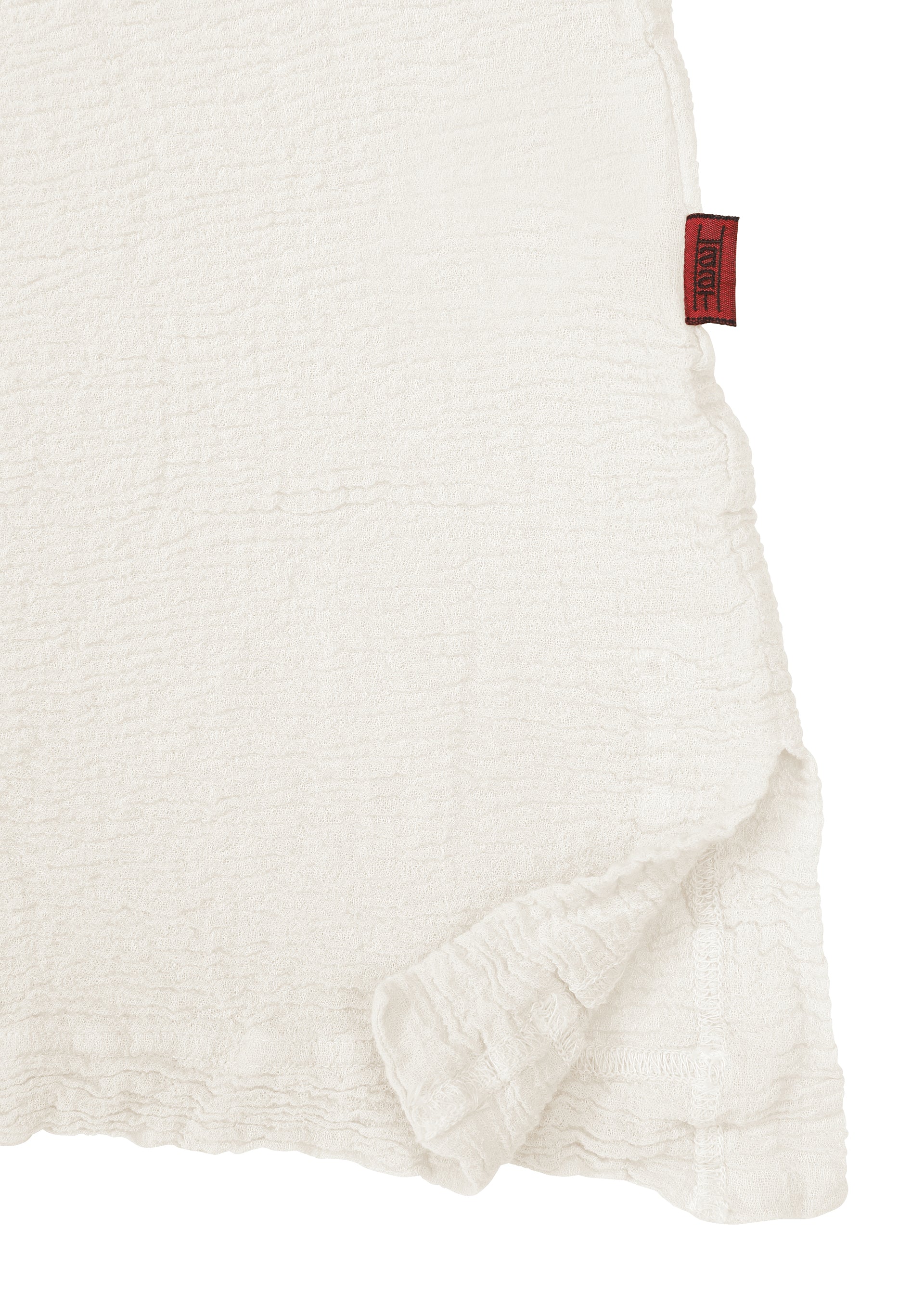 Zoomed view A close-up of the white textured fabric from the HaaT KYO CHIJIMI 2WAY JUNE 1 shirt highlights a slightly ruffled edge and a small red tag on the upper right seam, showcasing details created by product dyeing.