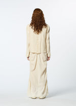 A person with long curly hair, wearing a textured cream-colored TENMOKU COTTON skirt and matching long-sleeved top by HaaT, stands facing away against a plain white background.