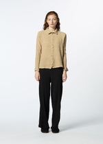 A person faces forward in a beige HaaT KYO CHIJIMI 2WAY JANUARY 2 long-sleeved shirt and loose black pants with black shoes, set against a plain white background.