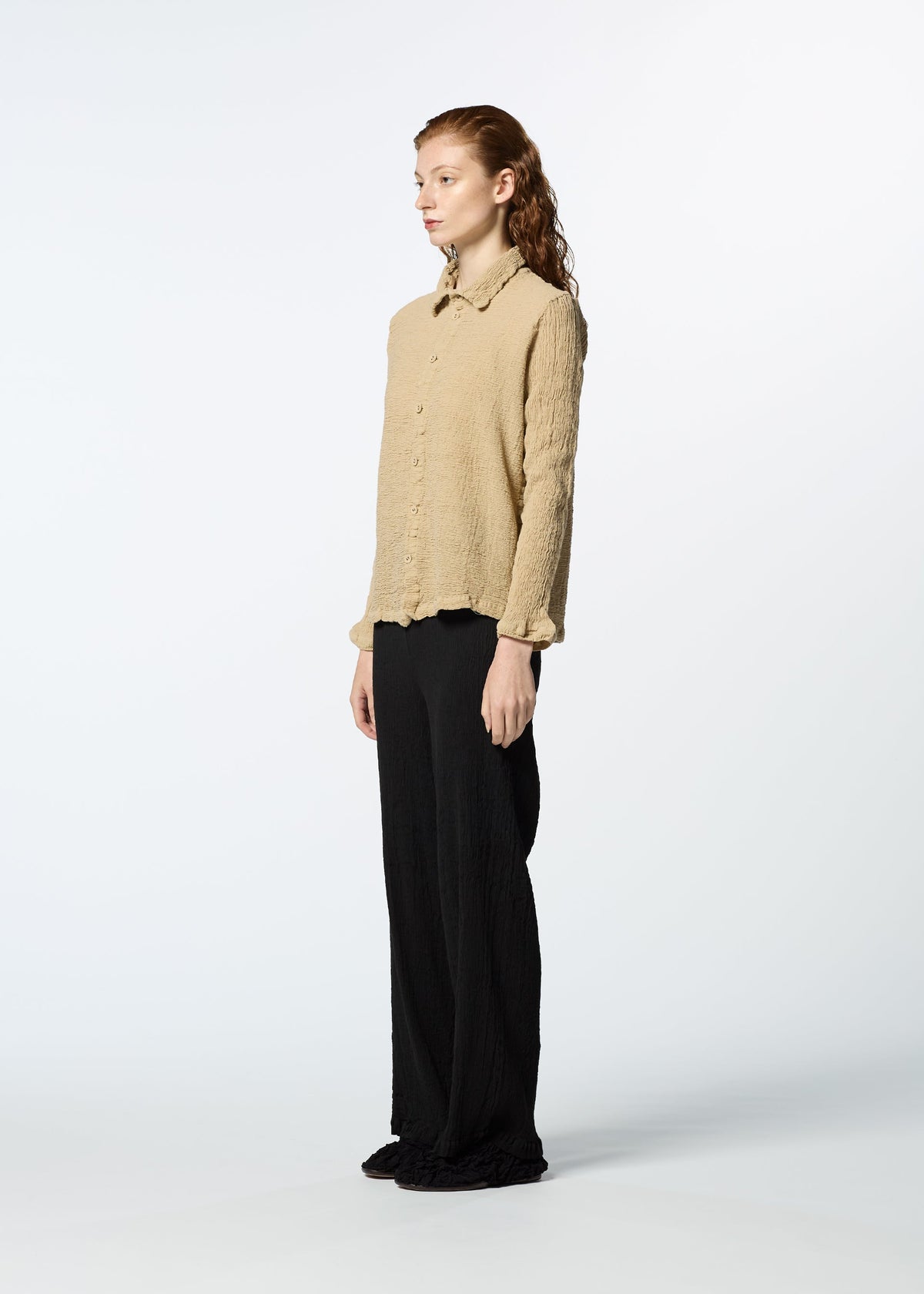 A person in profile against a white background wears HaaT's KYO CHIJIMI 2WAY JANUARY 2 long-sleeved shirt with textured fabric and loose black pants. Their hair is slicked back, and their expression is calm and neutral. view 5 of 7