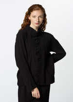 A woman with long, wavy red hair wears the HaaT TENMOKU COTTON black garment-dyed long-sleeve blouse with a ruffled front, made from textured stretchy fabric, standing against a plain white background with a neutral expression.