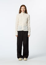 A person with long, wavy hair faces forward in a textured white long-sleeve top layered under the HaaT KUMO SHIBORI SHIRT, paired with loose black pants and off-white sneakers, set against a plain light background.