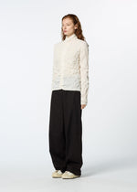 A person with long, wavy hair stands against a white background, wearing an off-white KUMO SHIBORI SHIRT by HaaT, loose black pants, and white sneakers.