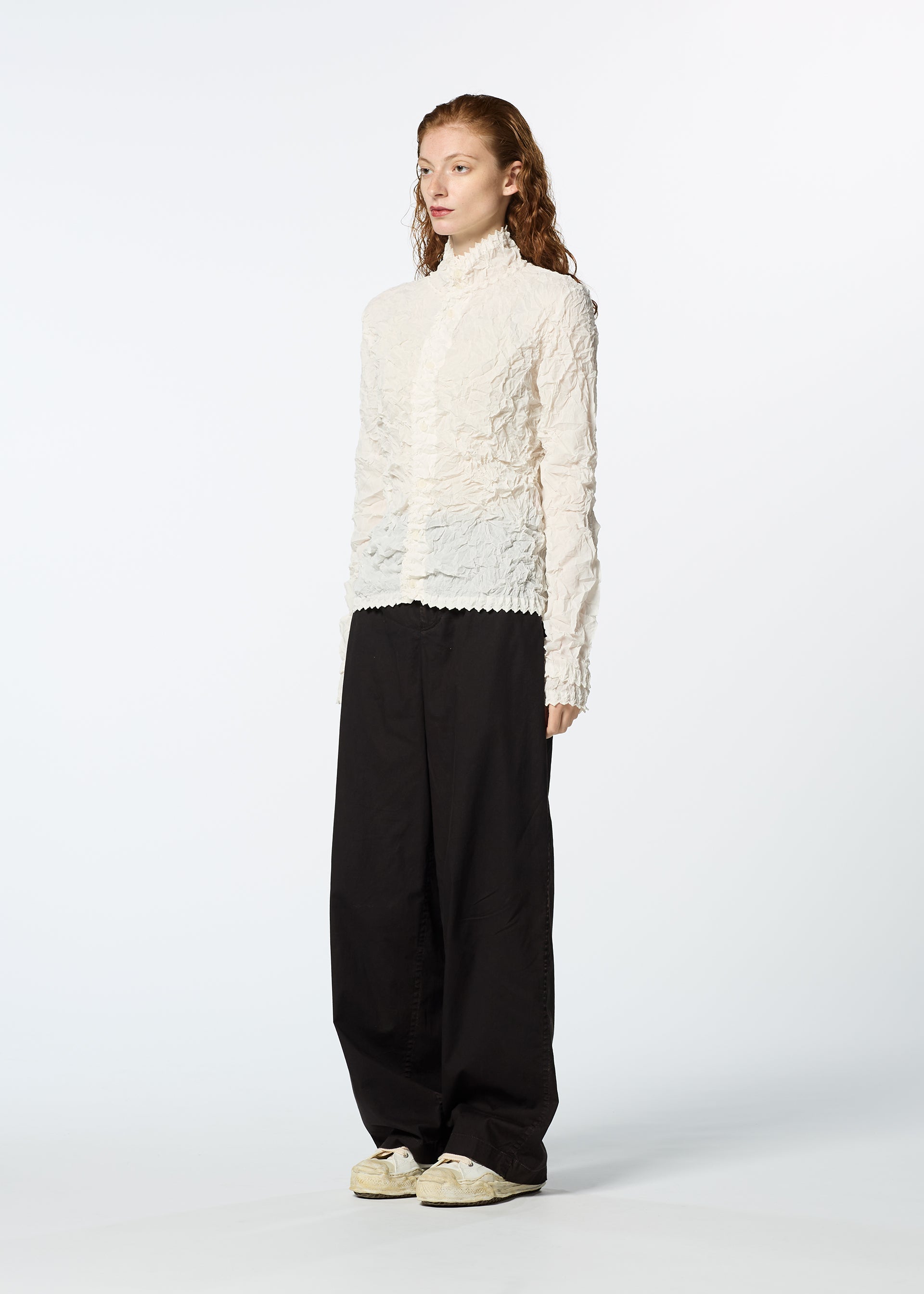 Zoomed view A person with long, wavy hair stands against a white background, wearing an off-white KUMO SHIBORI SHIRT by HaaT, loose black pants, and white sneakers.