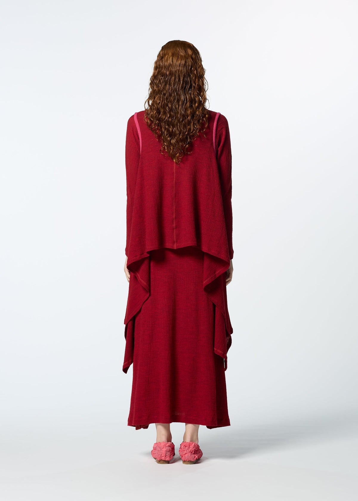 A person with long curly hair, seen from behind, wears HaaT's TRI COLOR WOOL dress in dark red with layers, paired with matching pink slippers, standing against a plain light background. view 8 of 8
