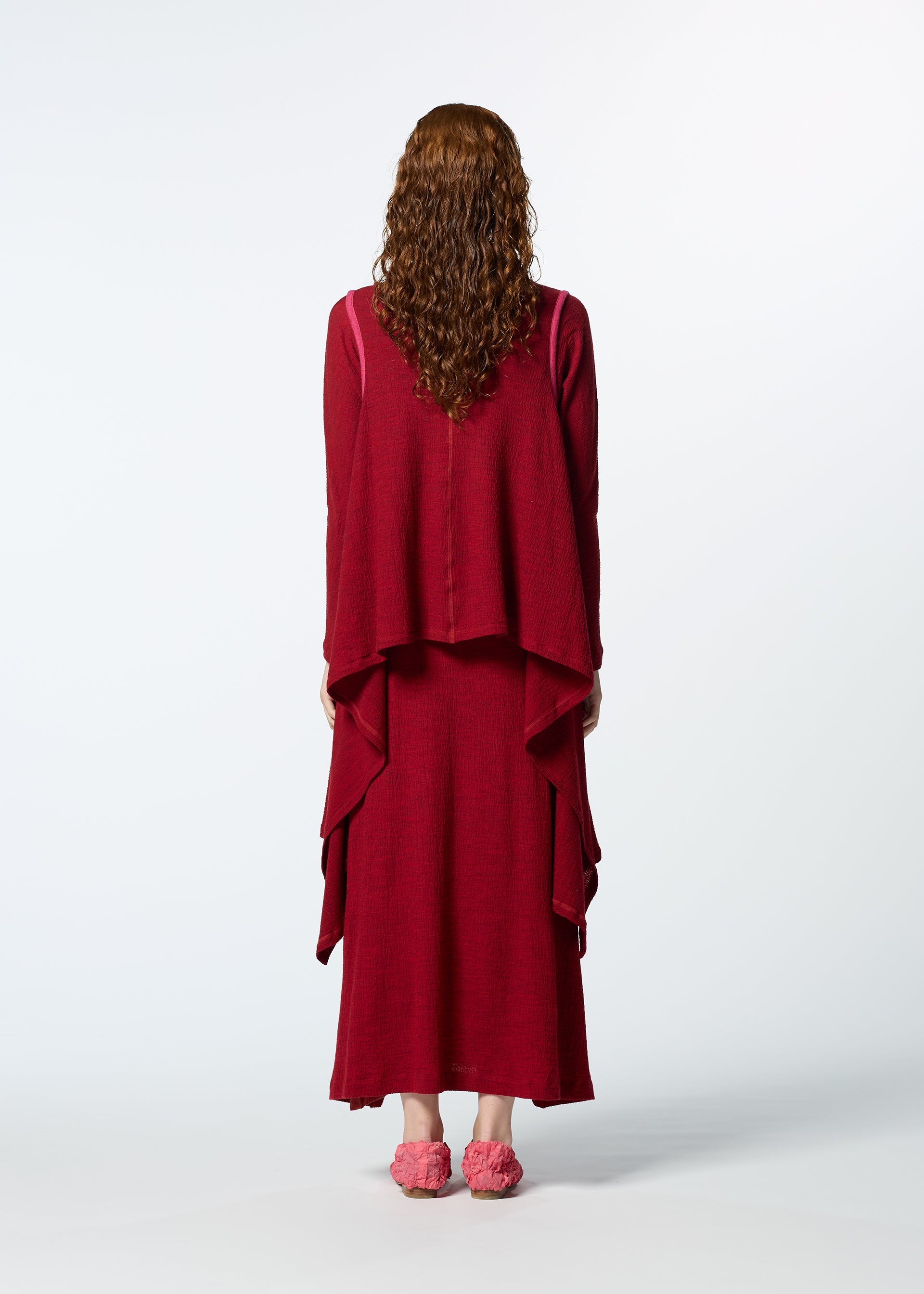 Zoomed view A person with long curly hair, seen from behind, wears HaaT's TRI COLOR WOOL dress in dark red with layers, paired with matching pink slippers, standing against a plain light background.