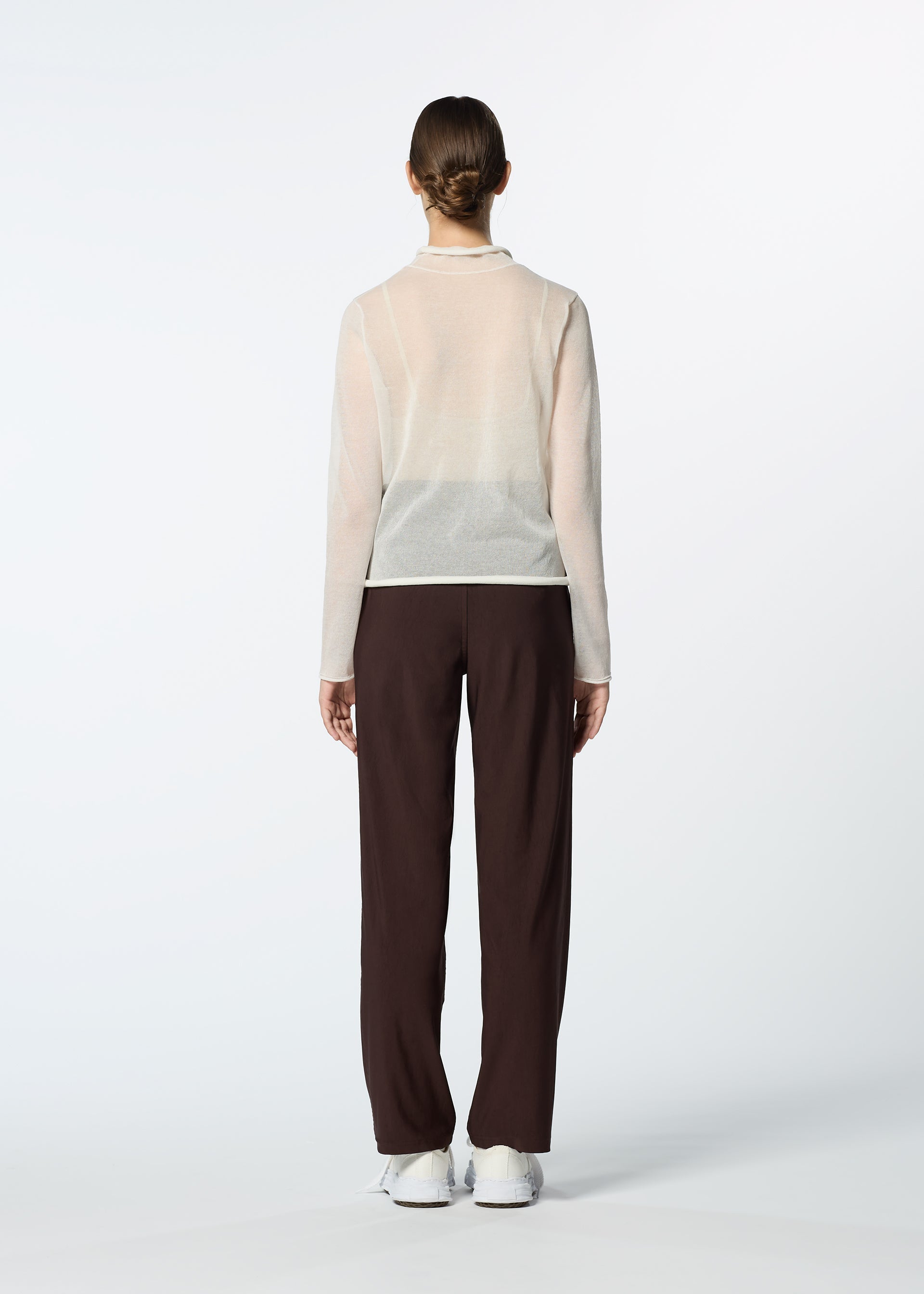 Zoomed view A person stands facing away, wearing HaaT’s NYLON STRETCH BOTTOM pants with a sheer long-sleeve beige top and white shoes against a plain light background.
