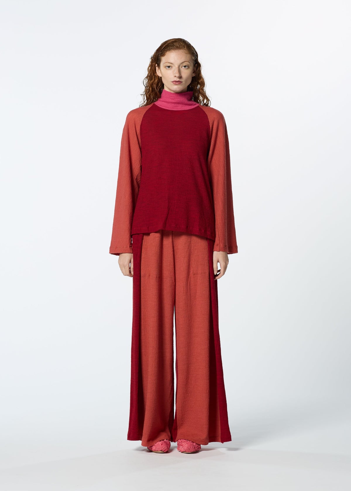 A person with long, curly hair wears the HaaT TRI COLOR WOOL top in maroon with wide-legged rust pants and pink shoes, styled against a plain light background. view 10 of 16