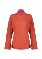 The HaaT TRI COLOR WOOL is a loose-fitting, long-sleeved orange merino wool top featuring a high pink collar with a single pink button, shown against a white background.
