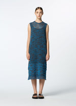 A young woman with straight brown hair stands facing forward, wearing HaaT's MELANGE MESH sleeveless blue knit dress with a textured pattern and fringe hem, paired with black open-toe sandals against a plain white background.
