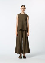 A young woman stands facing forward against a white background, wearing HaaT's RADIAL LINE KNIT sleeveless olive-green top in recycled polyester, with matching wide-legged pants and black sandals. Her hair is pulled back.