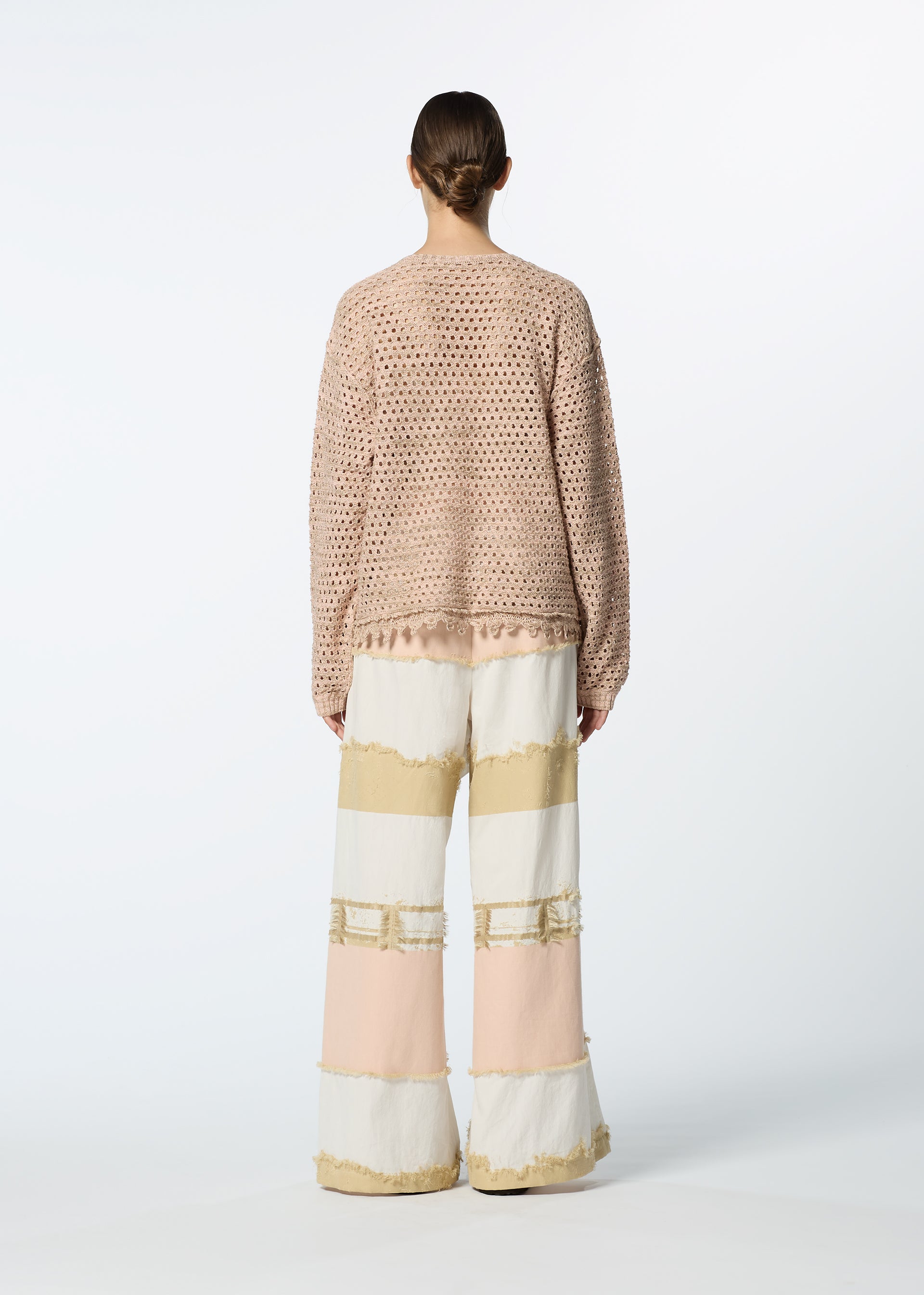 Zoomed view A person faces away, wearing HaaT's MELANGE MESH light pink mesh lace long-sleeve top and wide-legged, textured color-blocked pants in cream, beige, and blush. The background is plain white.