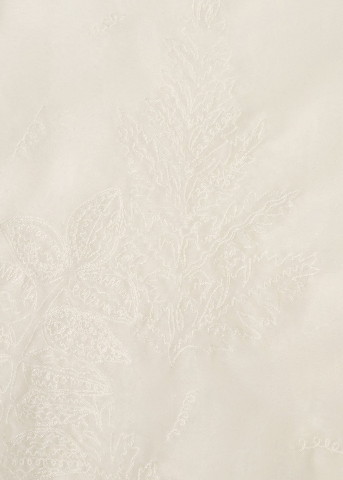 Close-up of GLASSLEAF by HaaT: white fabric featuring delicate Bhill embroidery with a subtle fern and leaf motif, creating a textured, monochromatic botanical design on a smooth surface. view 5 of 8