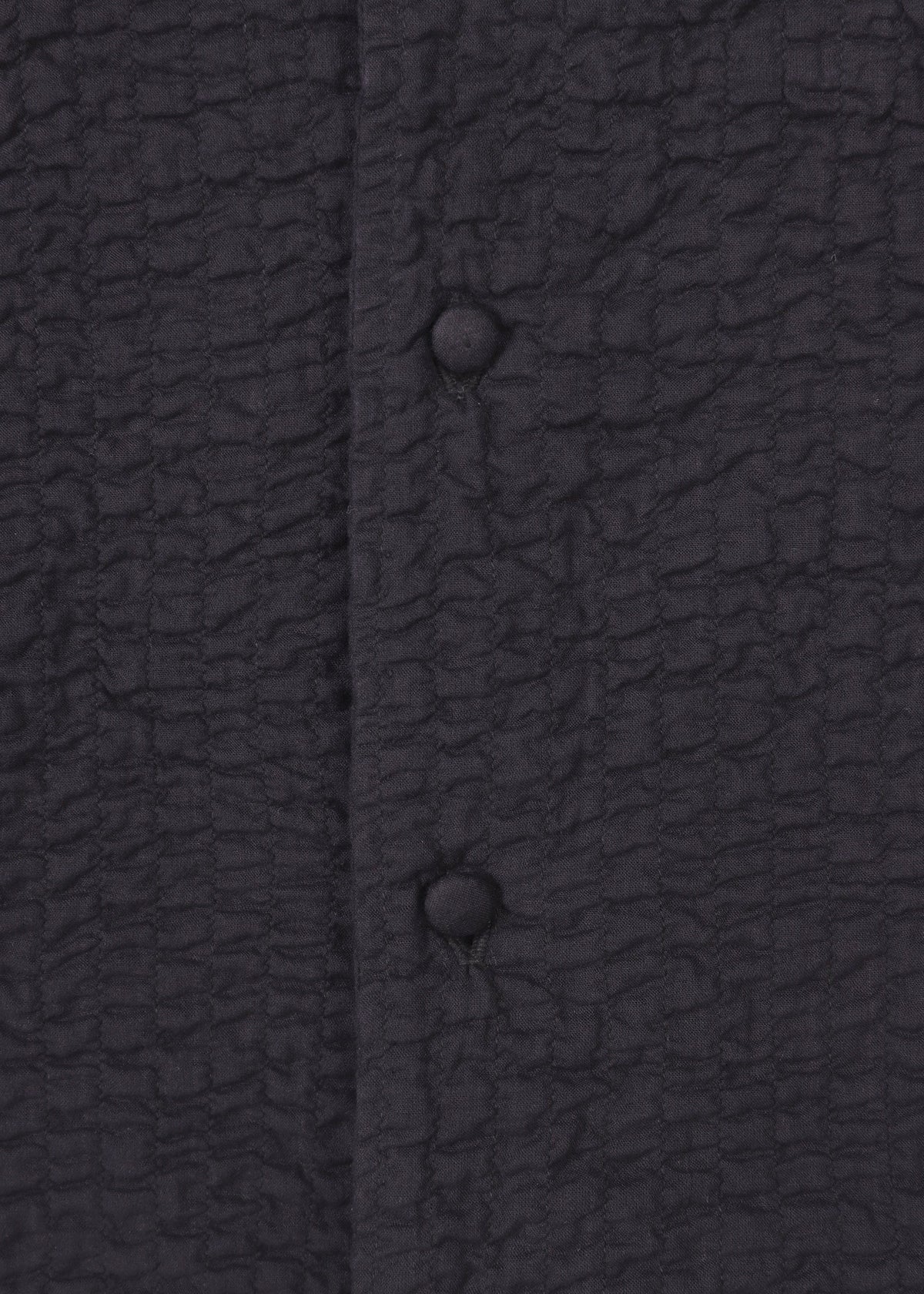 Close-up of the HaaT 3 MUL MACHINE KABIRA '26SS jacket in textured black with a crinkled pattern, vertical seam, and two fabric-covered round buttons, inspired by unisex silhouettes and subtle Indian embroidery. view 3 of 8