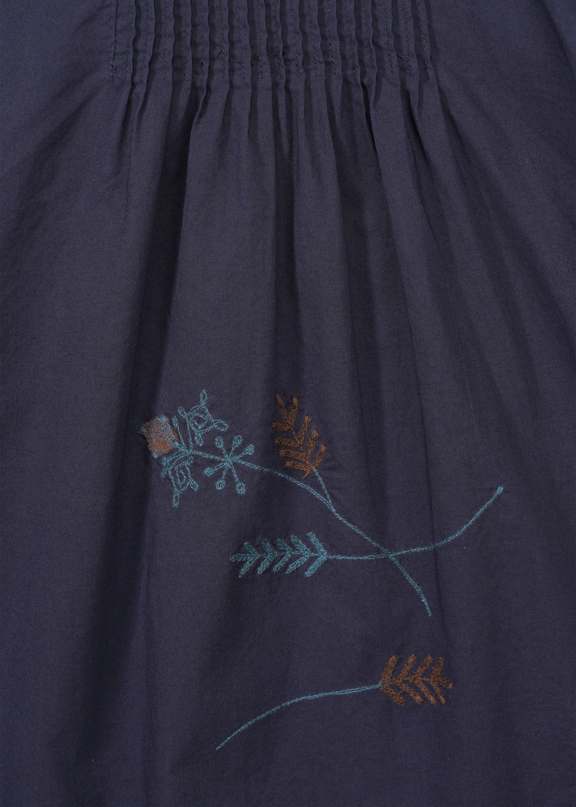 Zoomed view The DAMI LEAVES pants by HaaT are dark navy cotton with a gathered seam at the top and simple handmade Indian embroidery of light blue and brown floral and leaf motifs near the bottom center.