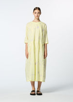 A woman stands against a plain background wearing HaaT’s DAMI LEAVES, a loose, light yellow handmade Indian dress with three-quarter sleeves and subtle floral patterns, paired with black flat sandals.