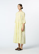 A woman in profile wears the DAMI LEAVES handmade Indian dress by HaaT—a loose, light yellow, mid-length piece with subtle Chikan embroidery—paired with black sandals, her hair tied back, set against a plain white background.