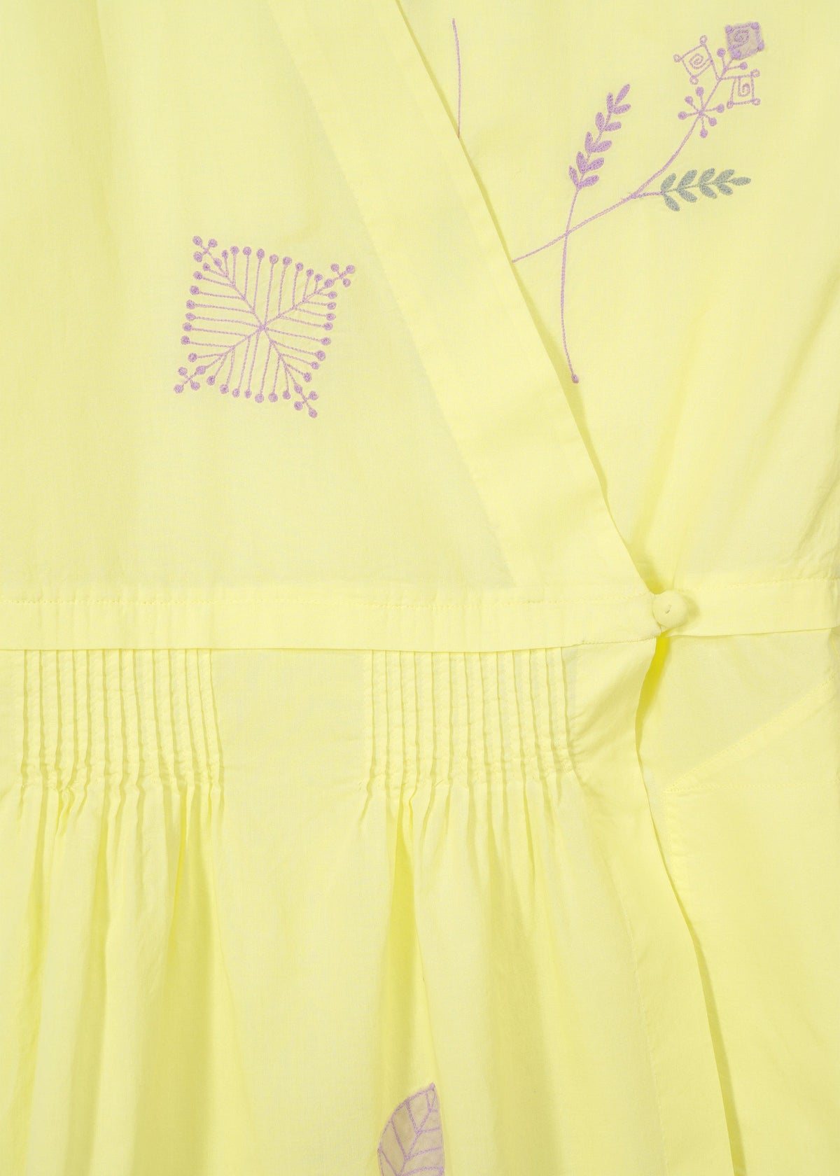Close-up of HaaT's DAMI LEAVES: a handmade Indian dress in light yellow with intricate purple geometric and floral embroidery, gathered pleats, and a fabric-covered button detail. view 6 of 9