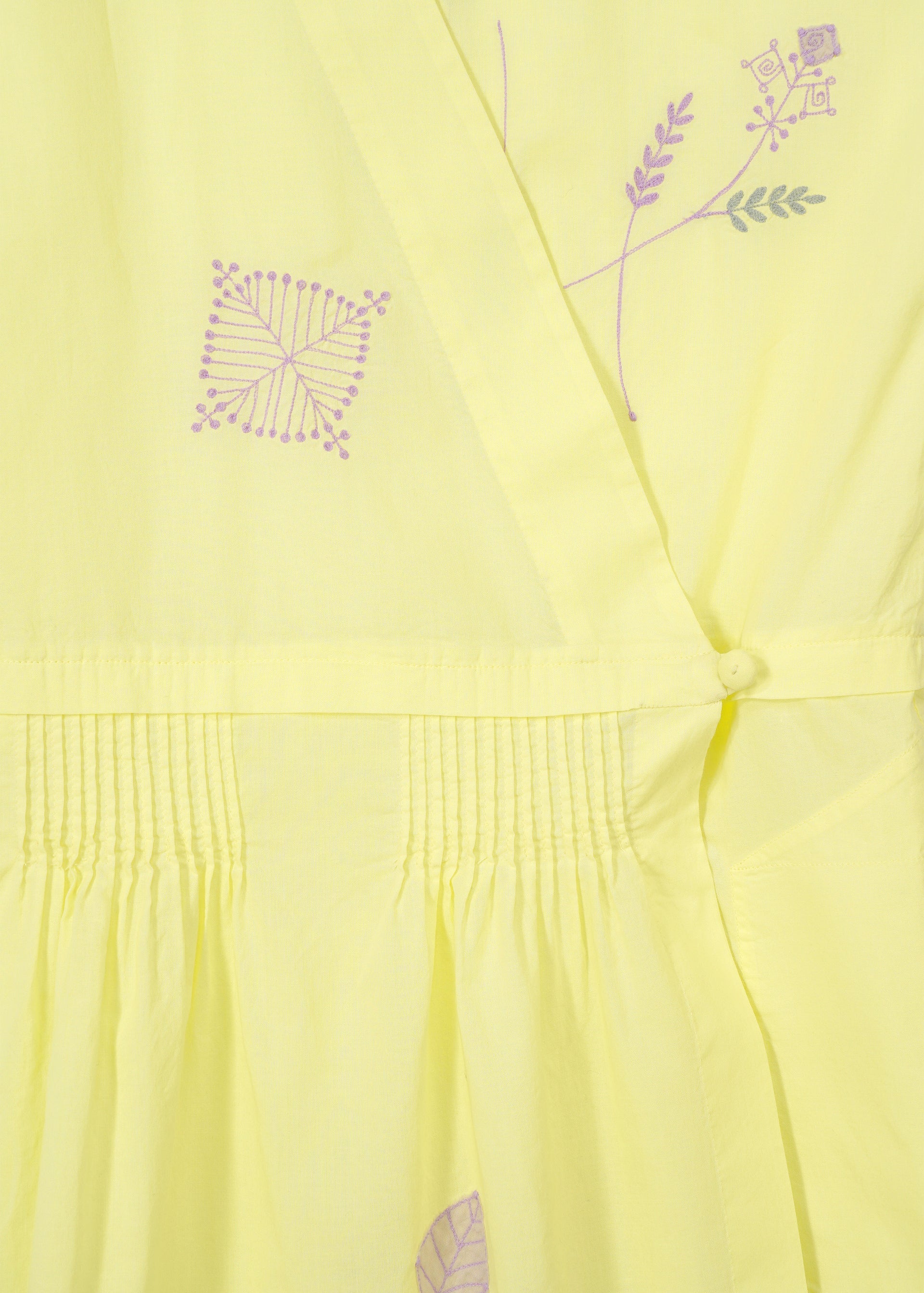 Zoomed view Close-up of HaaT's DAMI LEAVES: a handmade Indian dress in light yellow with intricate purple geometric and floral embroidery, gathered pleats, and a fabric-covered button detail.
