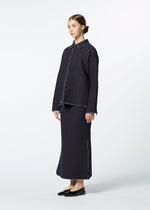 A woman stands against a plain background in HaaT’s DUAL LAYER: a textured, dark navy button-up shirt paired with a matching long skirt. Her black flats, tied-back hair, and handwoven cotton jacket complete the look.